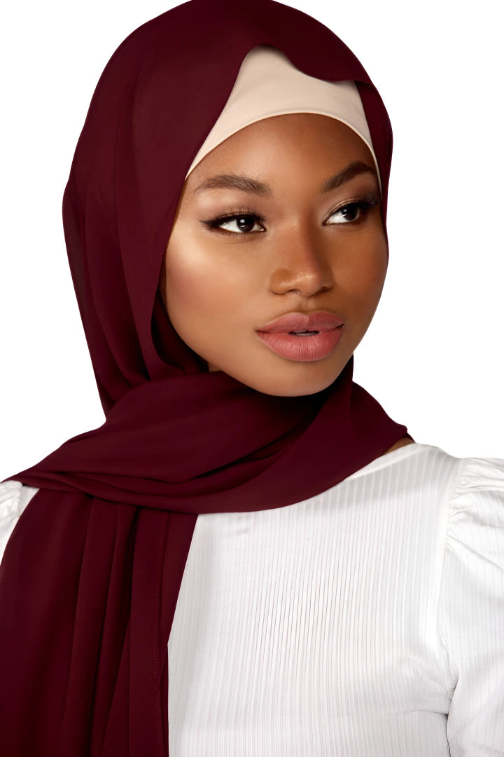 Woman wearing a burgundy hijab and white top on a plain background