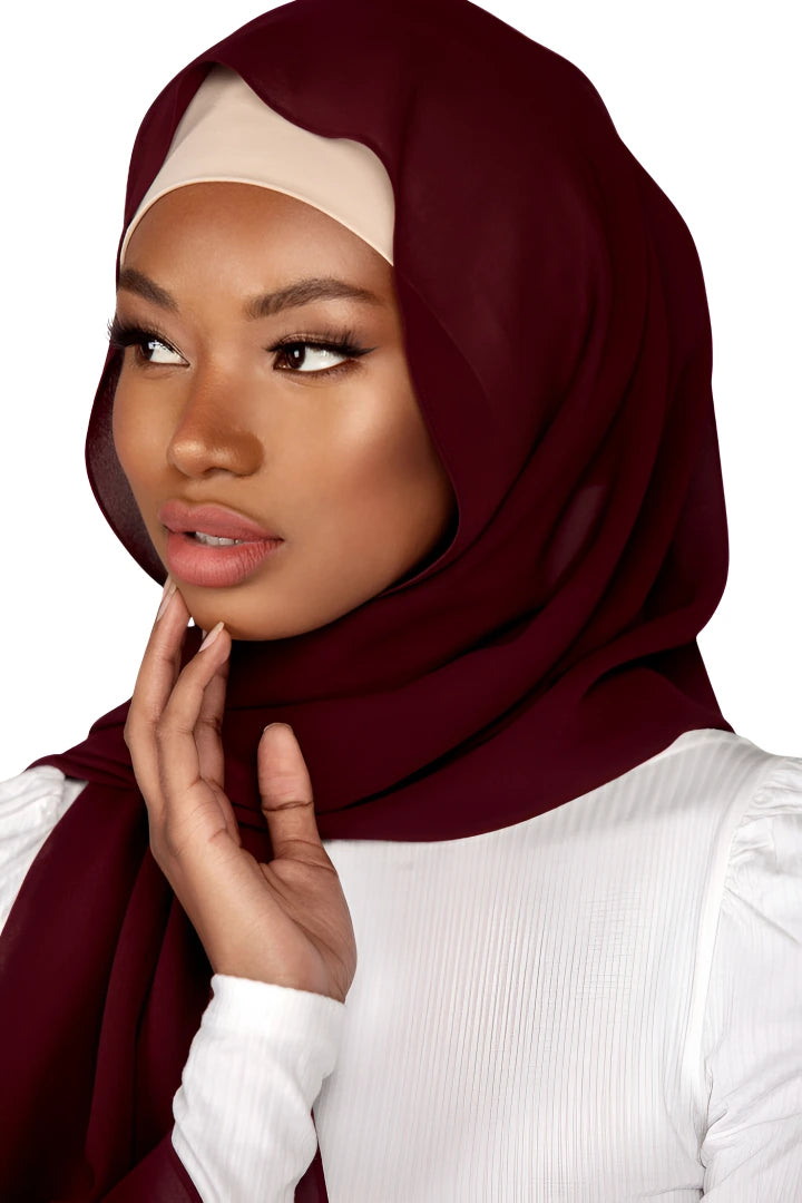 Woman wearing a burgundy hijab and white top on a plain background