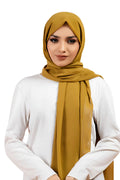 Woman wearing a mustard hijab and white top on a white background