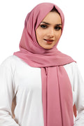 Woman wearing a pink hijab and white top on a white background