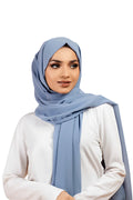 Woman wearing a light blue hijab and white shirt on a white background
