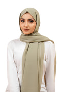 Woman wearing a beige hijab and white top on a white background