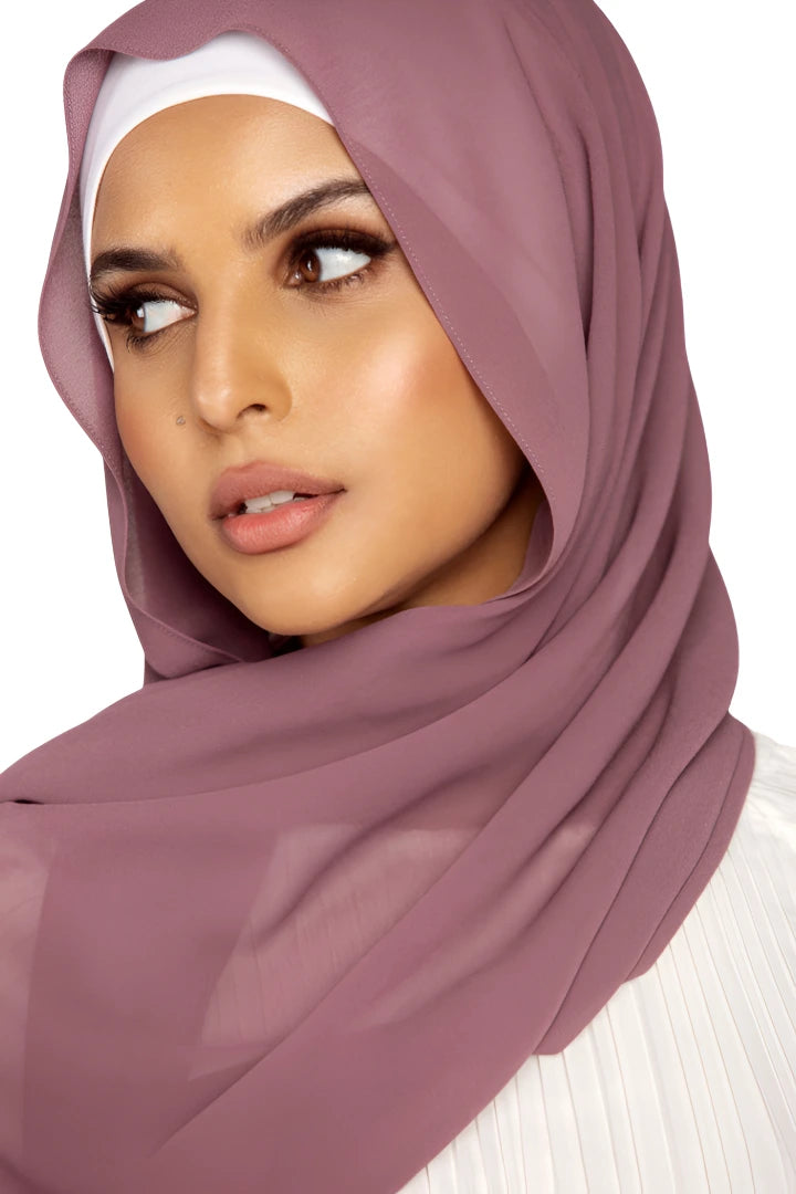 Woman wearing a mauve hijab and white top on a white background