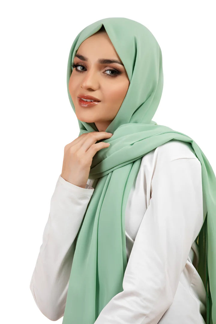 Woman wearing a light green hijab and white top on a white background